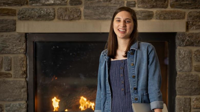 A female stands in front of a fireplace holding a laptop.