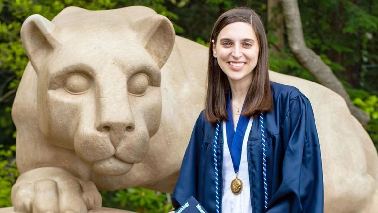 Dana Hallahan in blue cap and gown next to Nittany lion shrine at Penn state university park