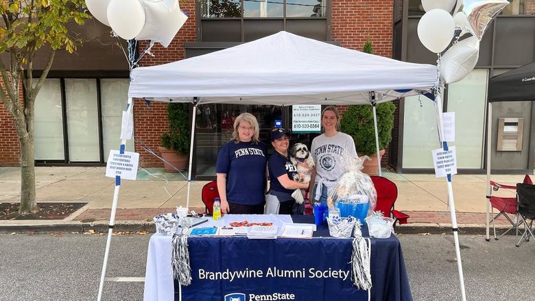 three women standing under a white tent, tablecloth says Brandywine Alumni Society
