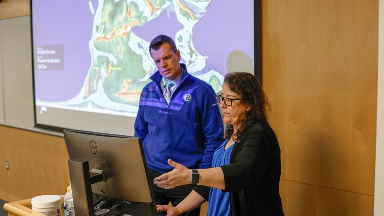 A professor points to a computer to explain an earthquake to a television news reporter.