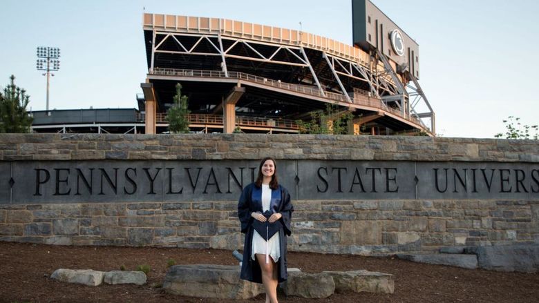 person in cap and gown in front of sports stadium