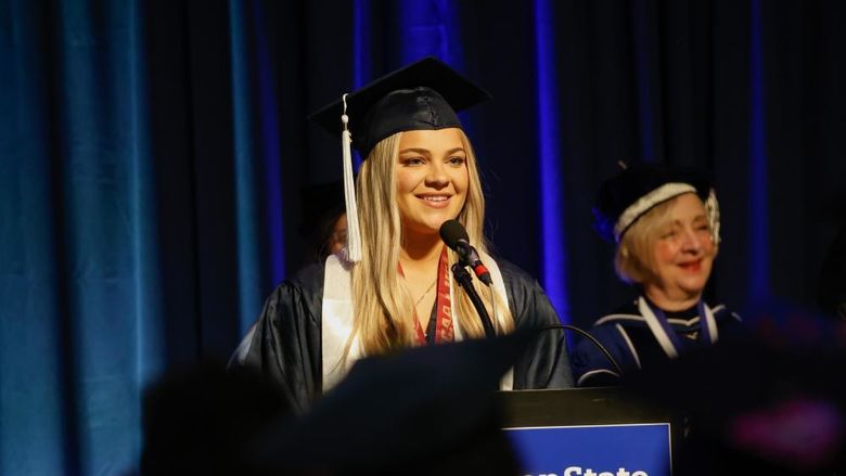 A person wearing a graduation gown stands at a lectern to speak at commencement.