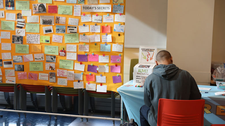 Student writing notecard for "Share a Secret" wall display