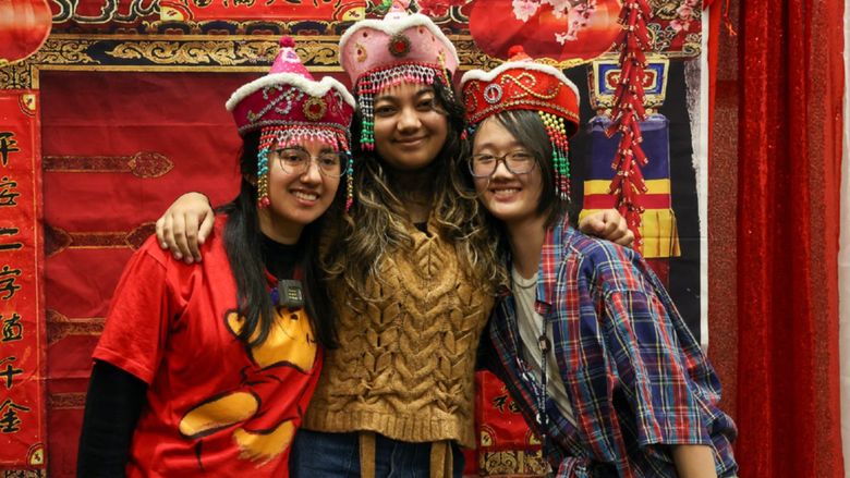 three students posing for photo with a Chinese new year backround of red and gold