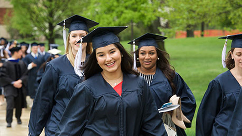 Female students in academic regalia walk to graduation