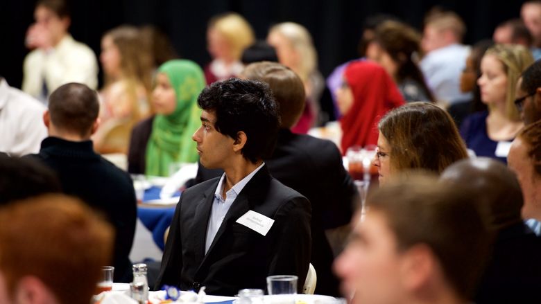 Student sitting at a table listening to a speech.