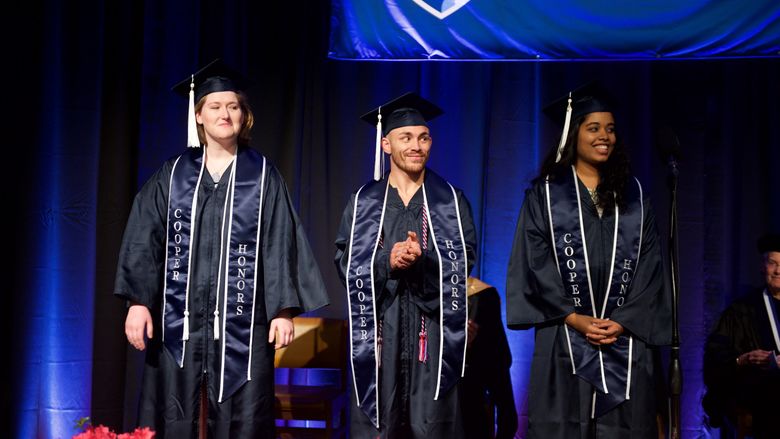 Three students at graduation stand on stage in academic regalia