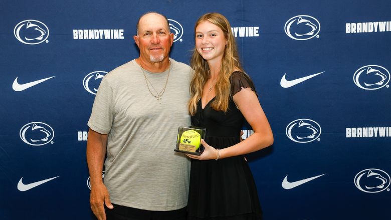student holding softball with coach