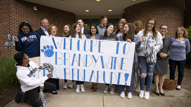 A group of 15 people stands behind a banner.