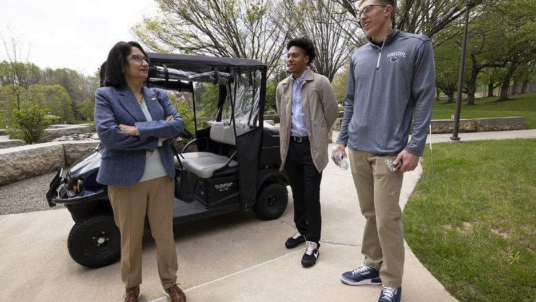 A woman and two men stand next to a golf cart.