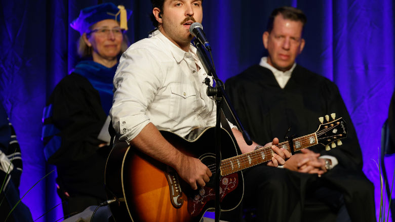 A student plays guitar and signs during Brandywine's commencement ceremony.