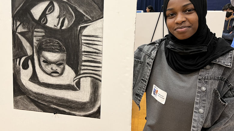 A woman stands next to her artwork.
