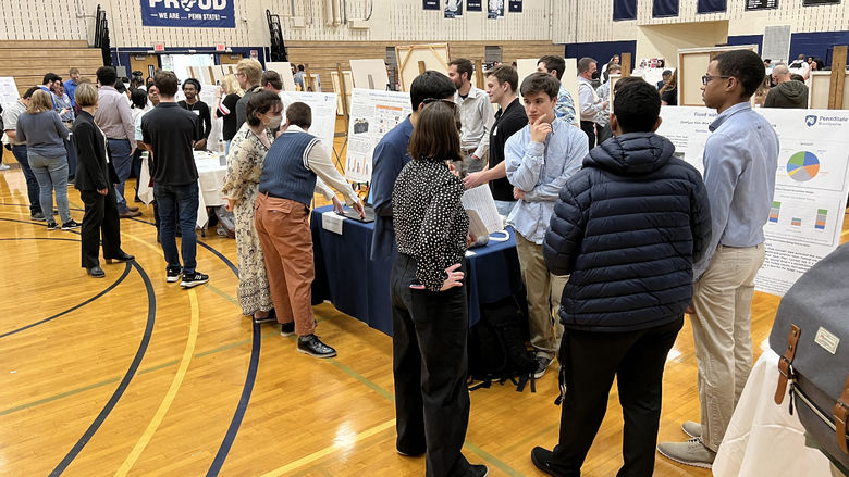 A crowd of people in the campus gym talk with students and look at research posters.