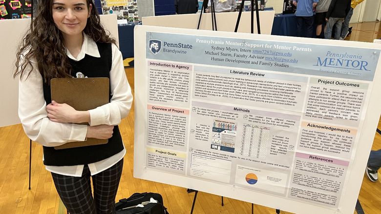 A student stands next to a poster about her internship.