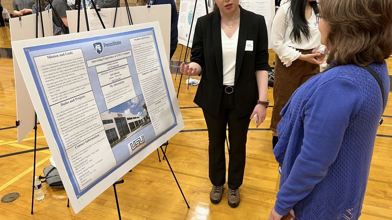 A woman stands next to her internship poster and explains it to another woman.