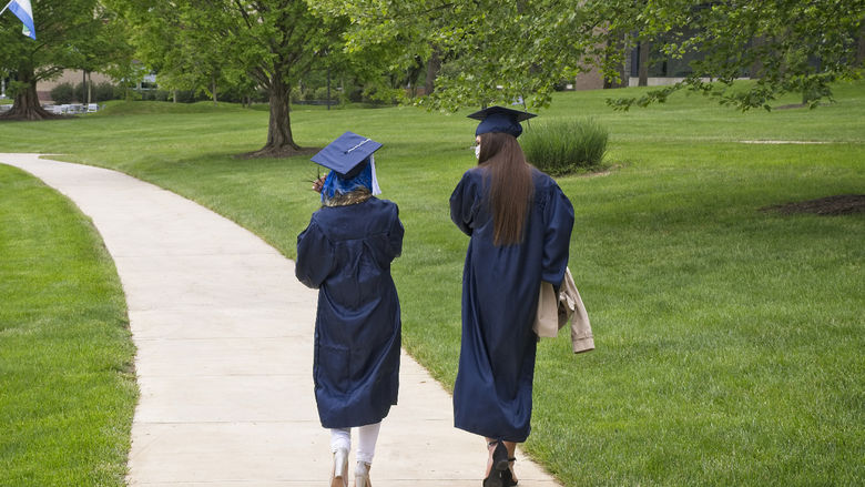 Two students walking while wearing commencement cap and gown.