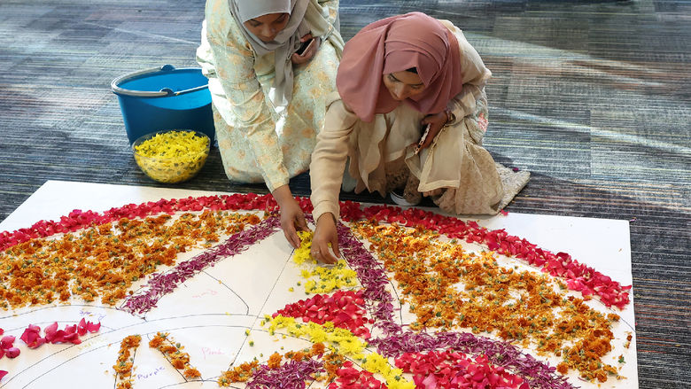 Two female students place flower petals onto the floor to create a rangoli.