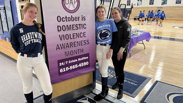 Three female students stand next to a banner that says October is Domestic Violence Awareness Month.