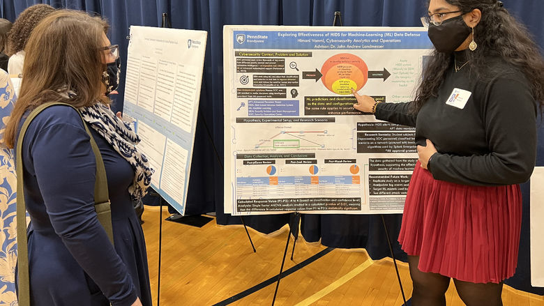 A women stands next to her research poster while explaining it to another woman.