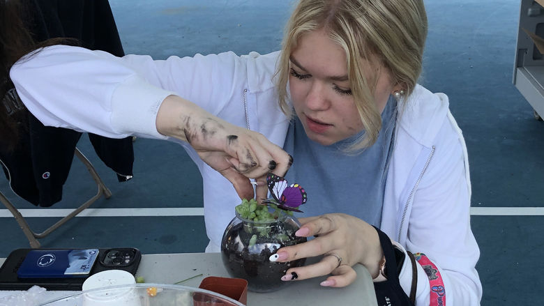 A student creates a mini-terrarium with a plant and small figurines.