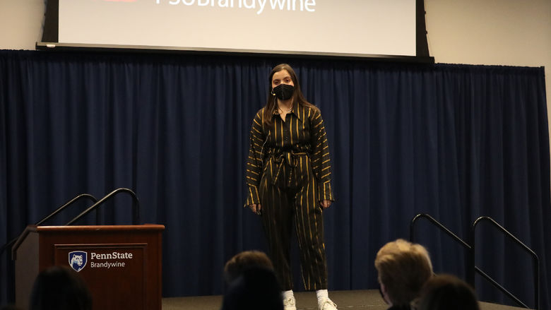 A female student stands on a stage speaking to an audience.