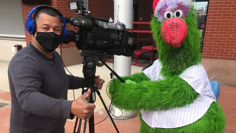 Man with camera wearing mask standing with Philly Phanatic