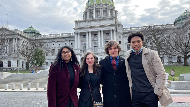 Four students stand in front of the Pennsylvania Capital Building