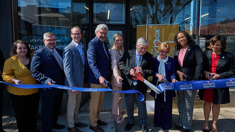 A group of 9 people cuts a long ribbon in front of a building.