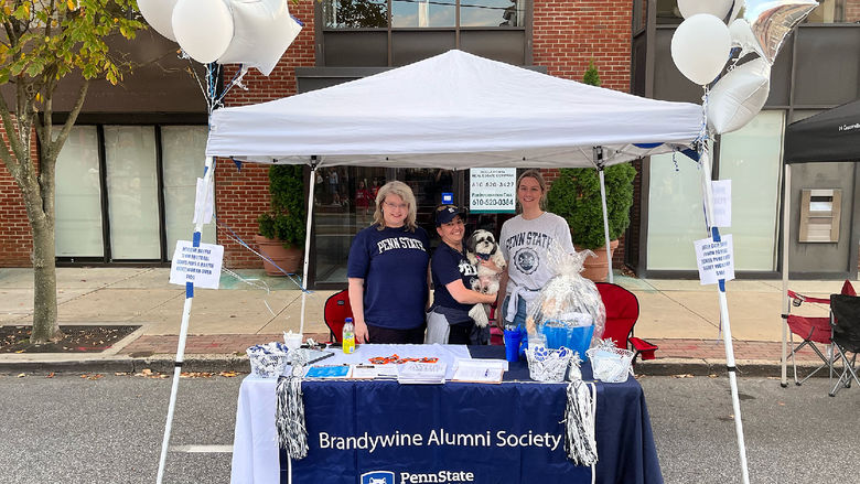 three women standing under a white tent, tablecloth says Brandywine Alumni Society