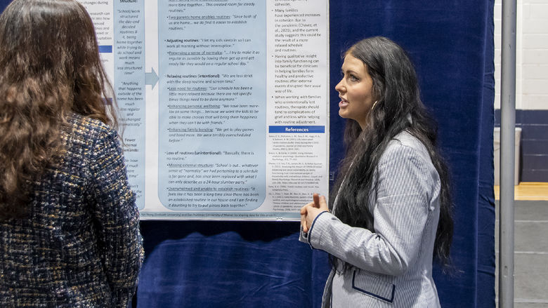 Young woman with long brown hair wears a gray blazer presenting research