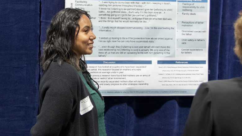 Girl with dark curly hair wearing a black cardigan presents research poster