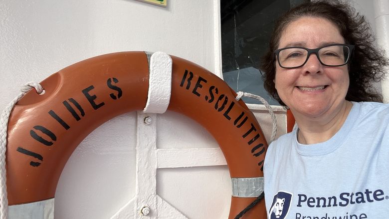 A woman stands next to a life preserver on a ship.