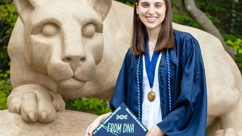 Dana Hallahan in blue cap and gown next to Nittany lion shrine at Penn state university park