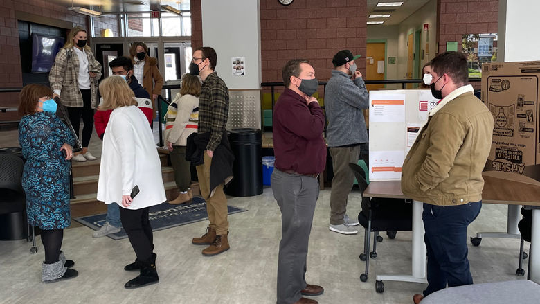 Students, faculty and staff gathered around posters in the lobby of a classroom building with large windows on Penn State Brandywine's campus.  