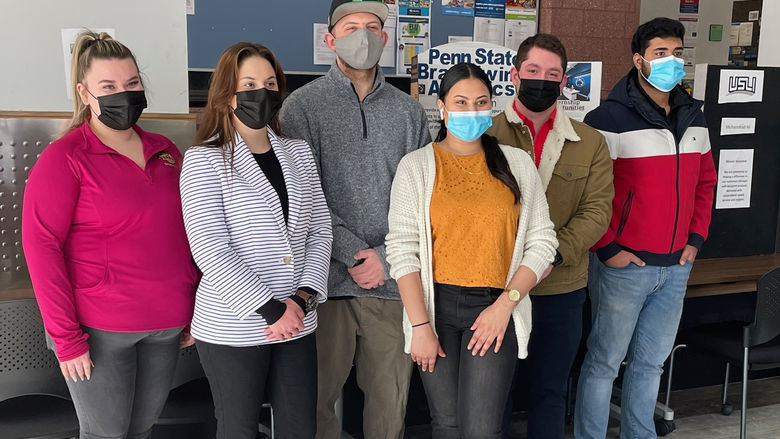 A group of students in masks standing in front of poster boards about their internship experiences. 