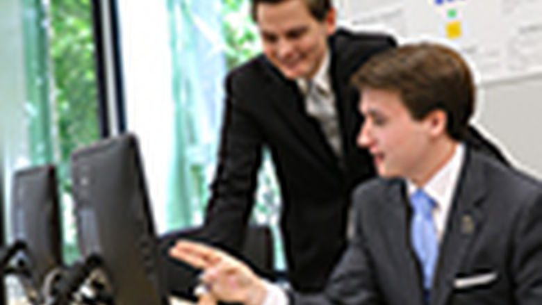 two male student interns at a computer in an office
