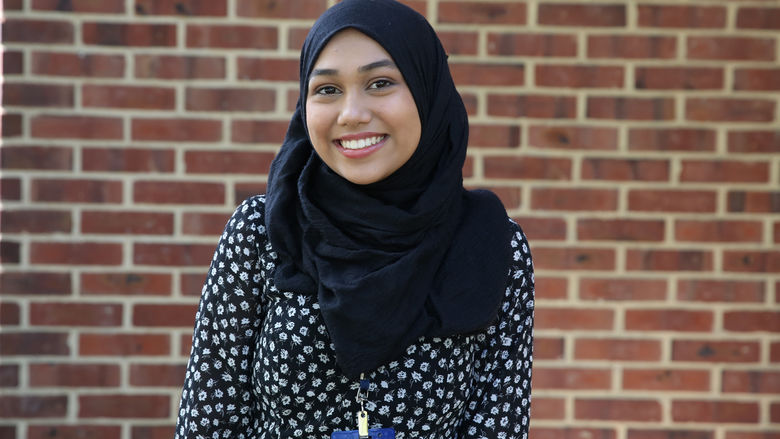 A student standing in front of a brick wall.