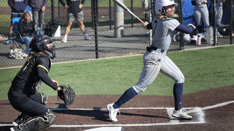 A female softball player swings the bat.