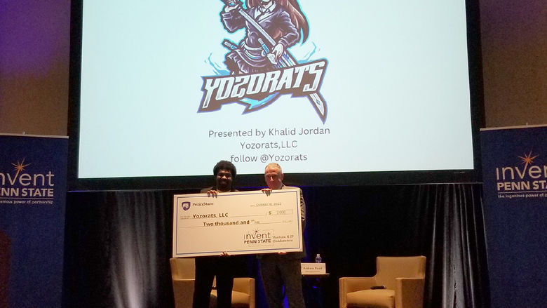 Khalid Jordan holding large check for $2000 with Invent Penn State representative