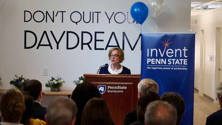 A woman stands at a lectern speaking to a crowd.