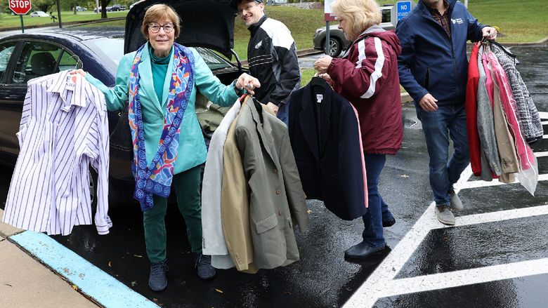 A man takes clothing out of a car trunk and hands it to three other adults.