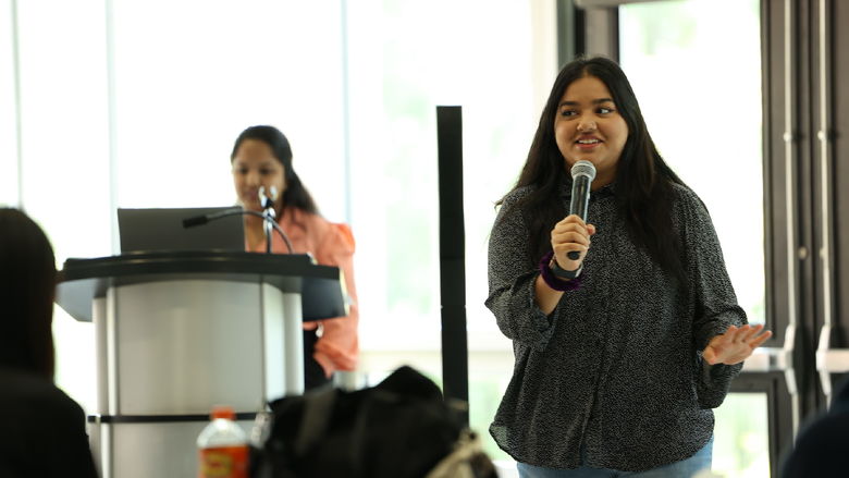 Girl holding a microphone with another girl at a podium