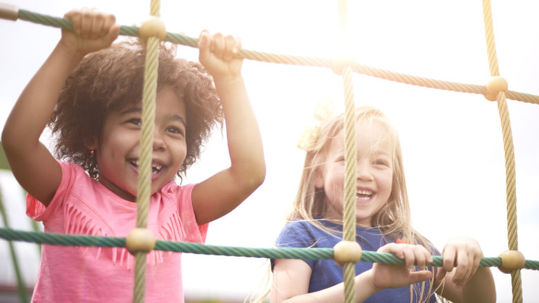 Two small children smiling and climbing on a rope course