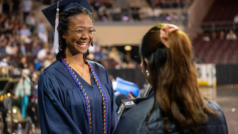 A Penn State Behrend graduate talks with a TV reporter before the college's commencement ceremony.