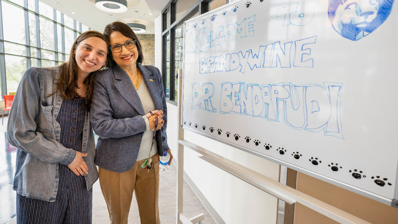 Two women stand next to each other in front of a whiteboard.