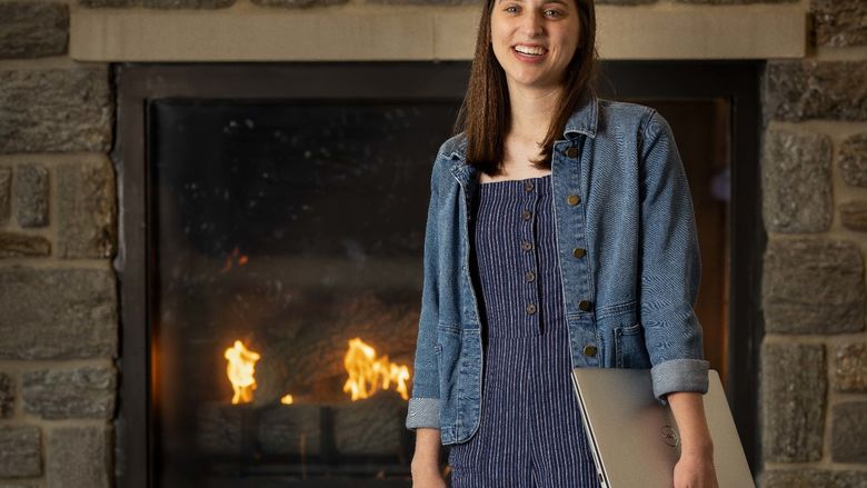 A female stands in front of a fireplace holding a laptop.
