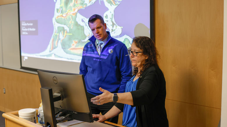 A professor points to a computer to explain an earthquake to a television news reporter.