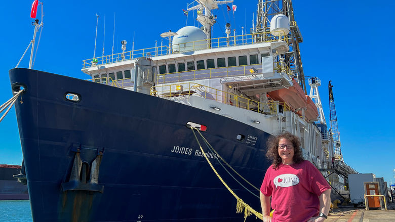 A woman stands on share next to a large ship.