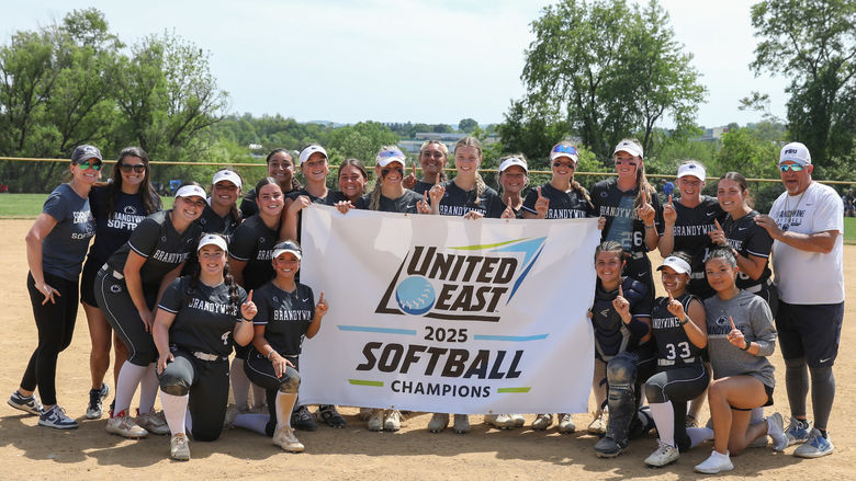 Penn State Brandywine's softball team holds the championship banner on the softball field.