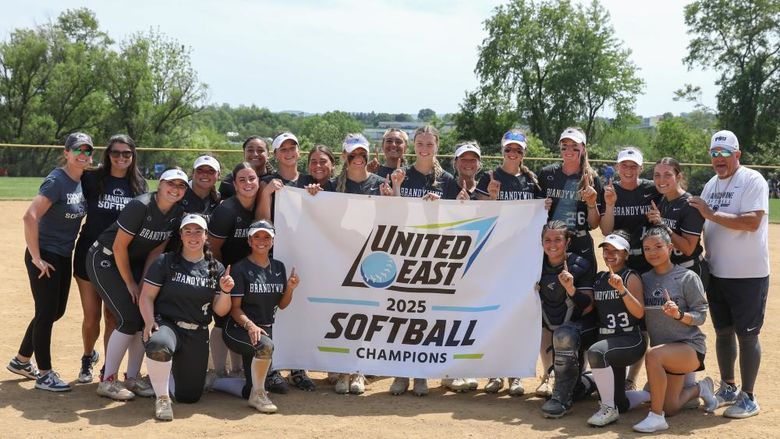 Penn State Brandywine's softball team holds the championship banner on the softball field.